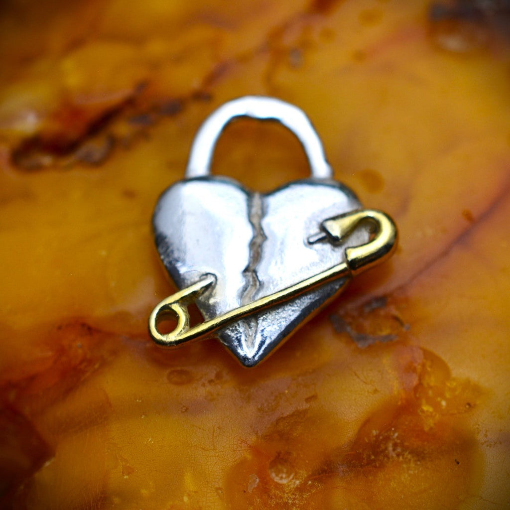 „Verletztes Herz“-Anhänger aus 925er Silber mit goldfarbenem Sicherheitsnadel-Akzent – Symbol für erlebten Schmerz und bleibende emotionale Spuren, Skulpturenschmuck im Boho- und rustikalen Stil | Art Diva