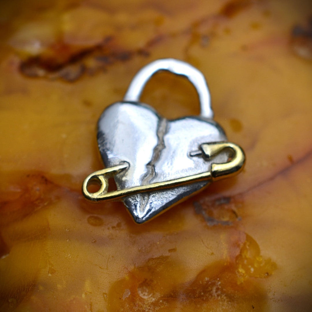 „Verletztes Herz“-Anhänger aus 925er Silber mit goldfarbenem Sicherheitsnadel-Akzent – Symbol für erlebten Schmerz und bleibende emotionale Spuren, Skulpturenschmuck im Boho- und rustikalen Stil | Art Diva