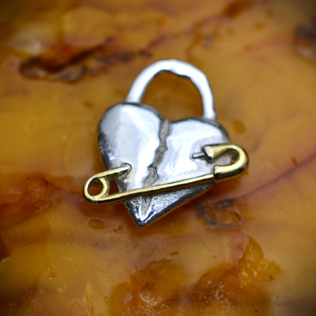 „Verletztes Herz“-Anhänger aus 925er Silber mit goldfarbenem Sicherheitsnadel-Akzent – Symbol für erlebten Schmerz und bleibende emotionale Spuren, Skulpturenschmuck im Boho- und rustikalen Stil | Art Diva